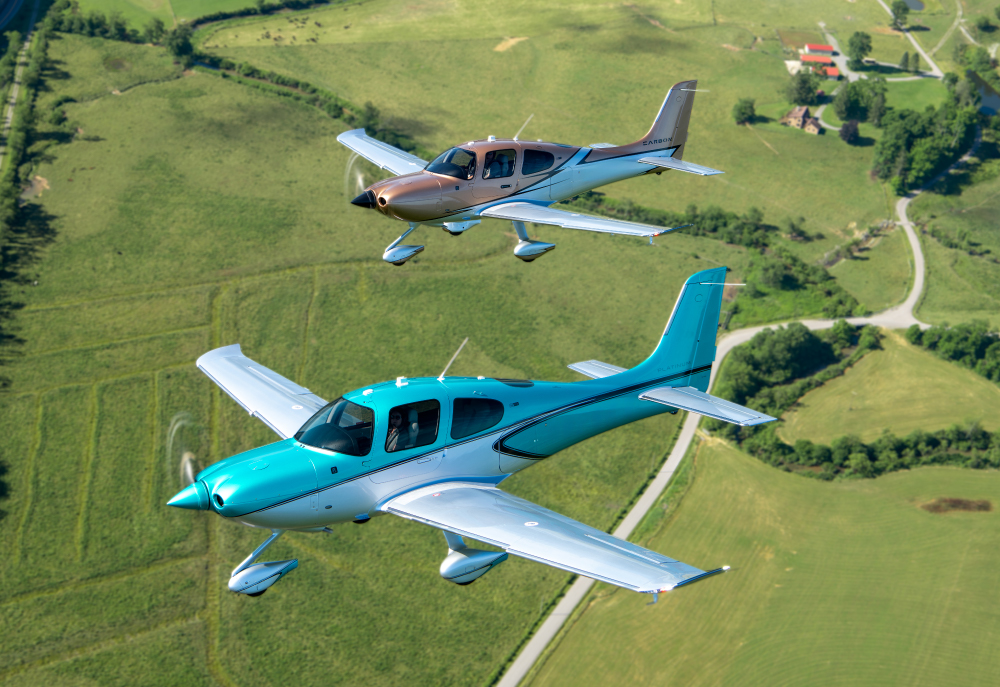 Two cirrus planes flying over green fields